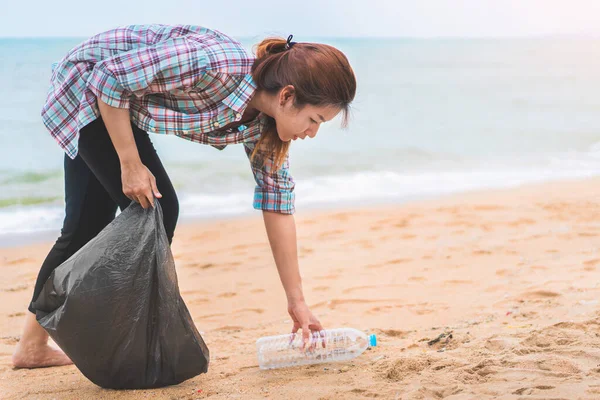 Asyalı bir kadın sabah plajı temizlemek için şişeyi plastik poşete koyup siyaha boyuyor. Gönüllü temizlik konsepti..