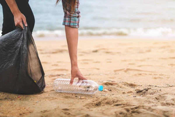 Asyalı bir kadın şişeyi plastik torbaya doldurup sabahları plajı temizlemek için siyaha boyuyor. Gönüllü konsepti..
