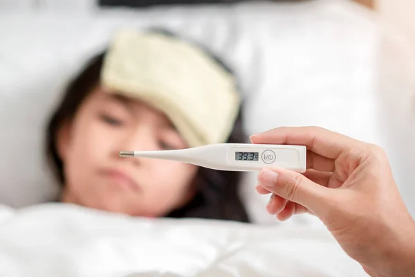 健康をチェックするための高温でデジタル温度計を保持しているアジアの母親彼女の娘 病気の子供は 高熱を減らすためのクールなタオルを持っています 手の焦点 健康と感染の概念 — ストック写真
