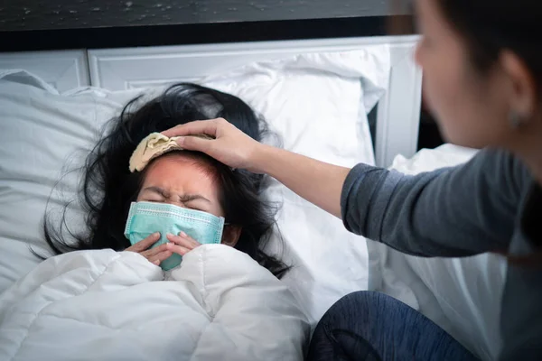 Asian mother take cool towel for reduce high fever on sick girl forehead, girl wearing medical protective face mask and coughing, Selective focus, Healthy and infection concept