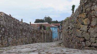 Ortaçağ Avrupa caddesi. Taş bloklardan geçen yol, alt manzara. Yol boyunca taştan yüksek duvarlar ve kiremit çatılı bebek evleri uzanıyor..