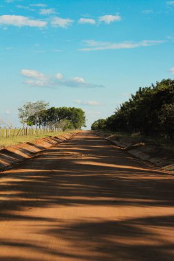 Kumun üzerinde gölgeler ve tepesinde mavi gökyüzü olan turuncu bir yolun manzarası.