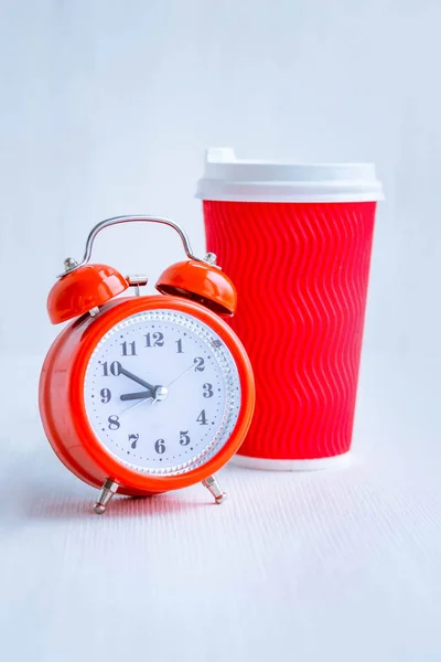 Red alarm clock and red paper cup of coffee. White background. Good morning. Morning coffee. Wake up in a good mood.