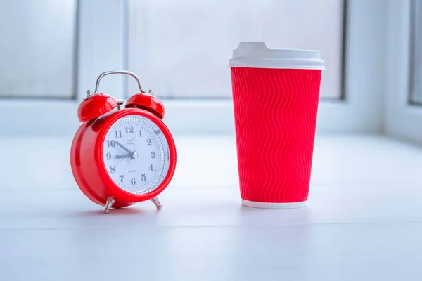 Red alarm clock and red paper cup of coffee. White background. Good morning. Morning coffee. Wake up in a good mood.
