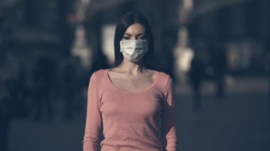 Tıbbi maskeli genç kadın kalabalık bir caddede duruyor.