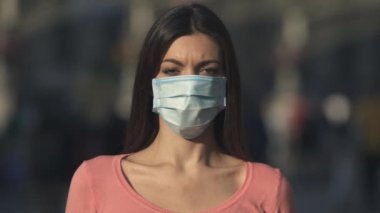 Tıbbi maskeli genç kadın kalabalığın içinde duruyor.