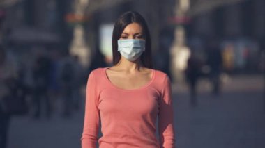Tıbbî maskeli kız kalabalık bir caddede duruyor.