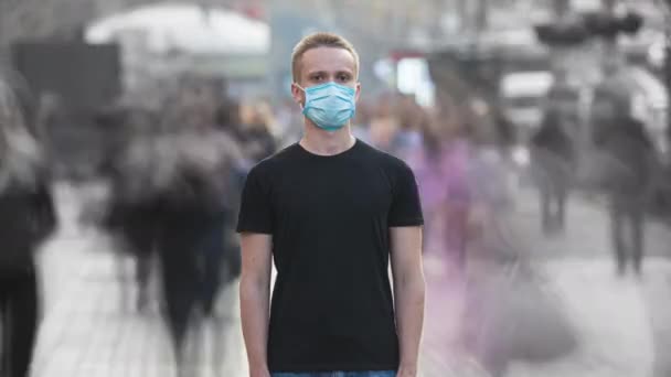 医者の顔のマスクをした若い男が群集の中に立っている 時間の経過 — ストック動画