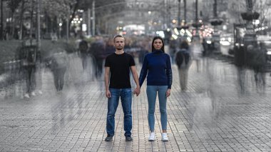 Erkek ve kadın kalabalık caddede durup el ele tutuşuyorlar.