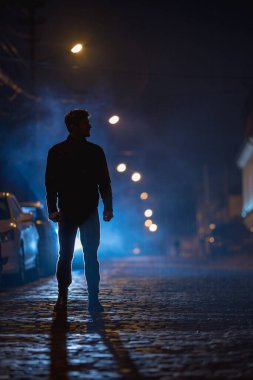 Adam sisli caddede duruyor. İyi akşamlar gece. Telefoto mercek görüntüsü