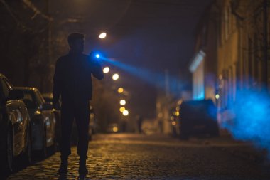Elinde fener olan adam yolda duruyor. Akşam vakti.