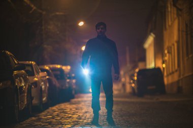 Elinde fener olan adam sokağı kontrol ediyor. Akşam vakti.