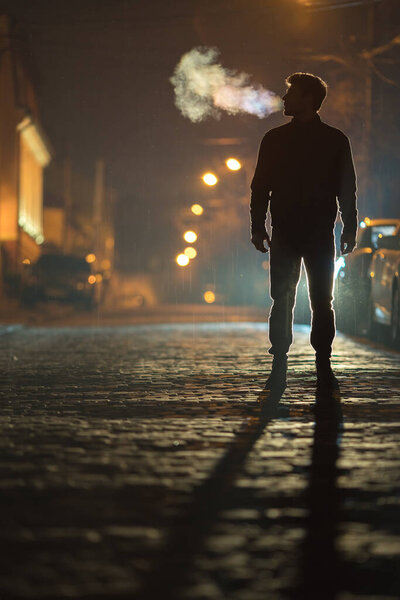 The man stand on the rain road. Evening night time. Telephoto lens shot