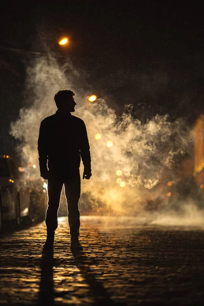 Adam duman sokağında duruyor. İyi akşamlar gece. Telefoto mercek görüntüsü