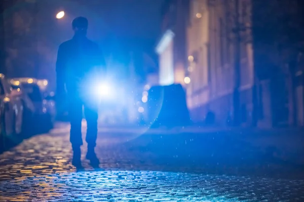 Elinde fener olan adam yolda duruyor. Akşam vakti.