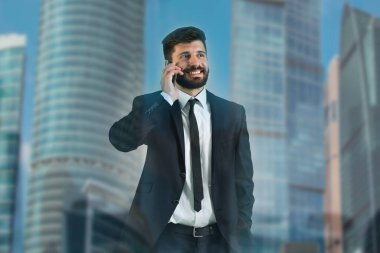 Bir gökdelenin arka planında pencerenin yanındaki adam telefonu.