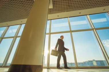 İş adamı arka planda bir bavulla yürüyor.