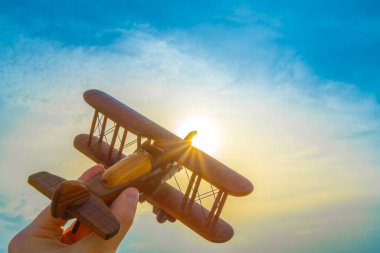 Gün batımının arka planında tahta bir uçak olan el.