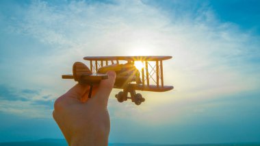 Gün doğumunun arka planında tahta bir uçak olan el.