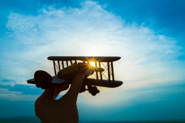 Gün doğumunun arka planında oyuncak bir uçak olan el.