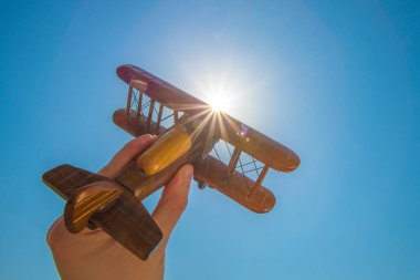 Güneşin arka planında tahta bir uçak olan el.