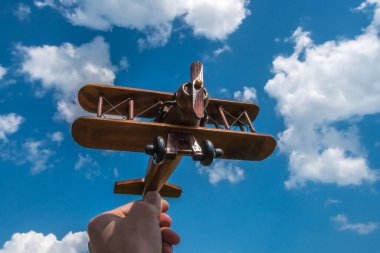 El, bulutun arka planında ahşap bir uçağı tutuyor.
