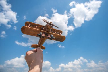 El, bulutların arkasında bir ahşap uçağı tutuyor.