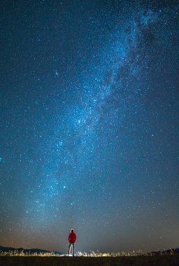 Adam yıldızların arka planında duruyor. Gece vakti.
