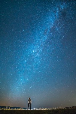 Adam yıldızların arka planında duruyor. Gece vakti.