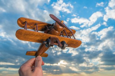 Mavi gökyüzünün arka planında ahşap bir uçağı tutan el.
