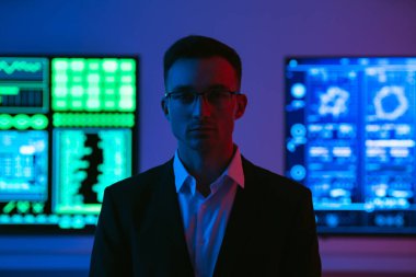 Arka planda duran gözlüklü adam.