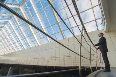 İş adamı ofis balkonunda korkulukların yanında duruyor.