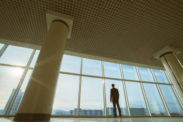 The businessman stand near panoramic window on the sunset background