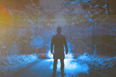 Adam karlı bir yolda, bir dumanın arkasında duruyor. Akşam vakti.