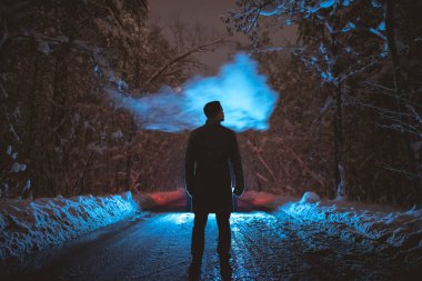 Ormandaki karlı yolda sigara içen adam. Akşam vakti.