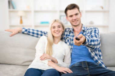 Mutlu adam ve kadın kanepeye oturur ve uzaktan kumandayı tutarlar.