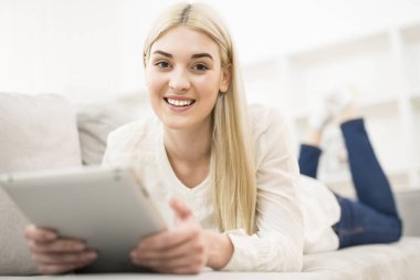 Gülümseyen kadın kanepeye uzandı ve bir tablet aldı.