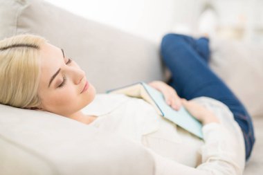 Kanepede uyuyan, elinde kitap olan genç kadın.