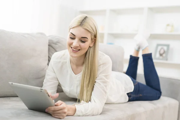 The happy woman lay on the sofa and hold a tablet