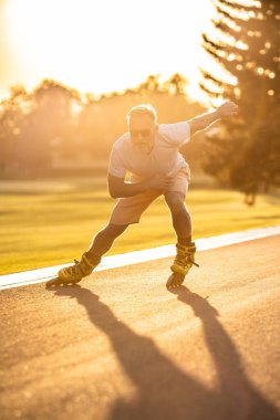 Güneş gözlüklü yaşlı adam gün batımında paten kayıyor.