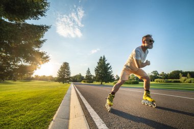 Güneş gözlüklü yaşlı adam yolda paten kayıyor.