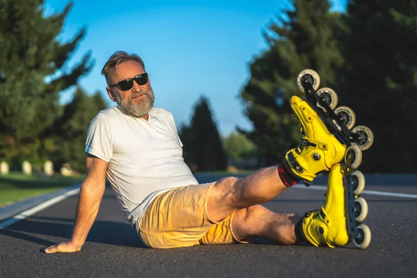 The old man with a roller skates sitting on the asphalt