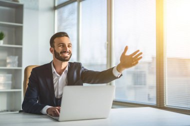 Masada oturan adam modern bir dizüstü bilgisayar ve el kol hareketi yapıyor.
