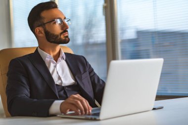 Masasında dizüstü bilgisayarla çalışan gözlüklü yakışıklı iş adamı.