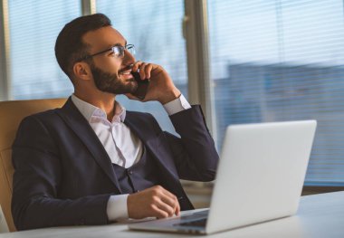 Gözlüklü işadamı masada oturuyor ve telefon ediyor.