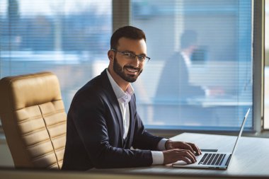 Masada dizüstü bilgisayarla çalışan gözlüklü mutlu adam.