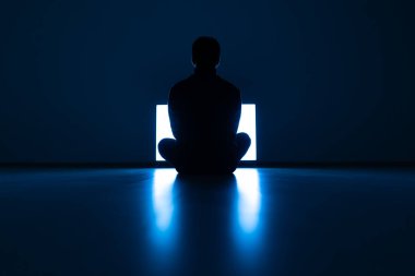 Erkek, karanlık odada televizyonun önünde yerde oturuyor.