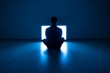 Erkek, karanlık odada televizyonun önünde yerde oturuyor.