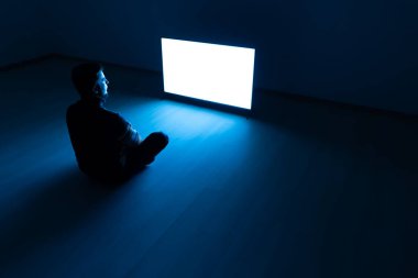 Karanlık odada televizyonun önünde oturan adam.