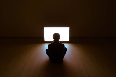 Televizyonun önünde yerde oturan adam.